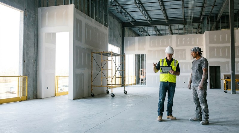 Drywall foreman reviewing a jobsite record on a tablet with a finisher